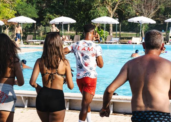 People at a pool with white umbrellas, trees in the background.