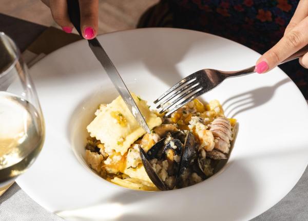 Piatto di ravioli di mare con un bicchiere di vino bianco.