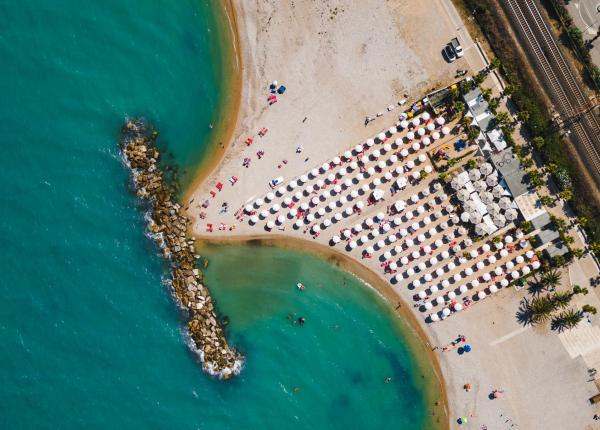 Spiaggia affollata con ombrelloni e mare turchese, vista dall'alto.