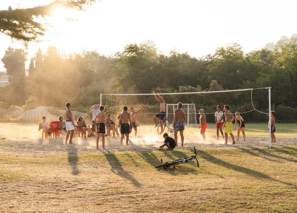 Giovani giocano a pallavolo sulla sabbia al tramonto.