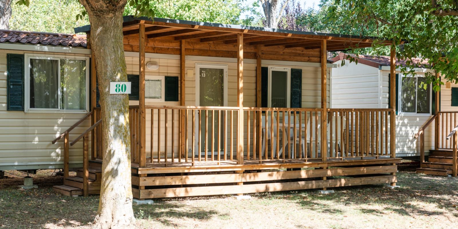 Mobile home with wooden porch, surrounded by greenery.