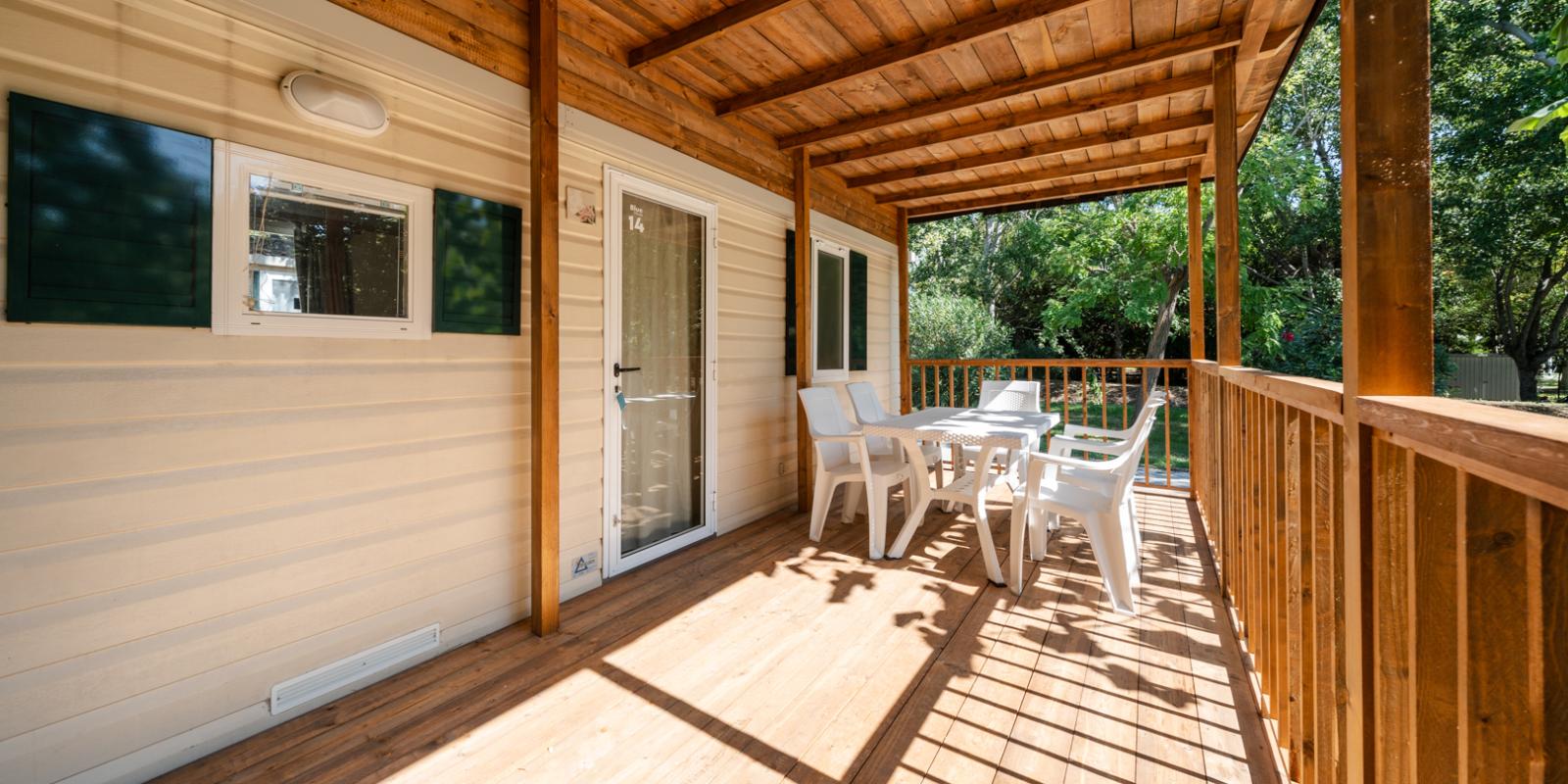 Wooden terrace with white table and chairs, surrounded by greenery.