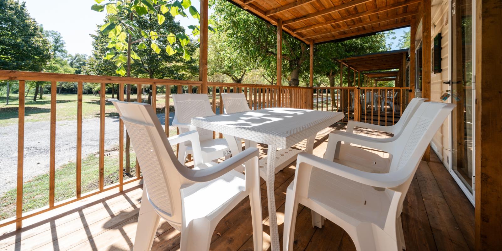 Wooden porch with white table and chairs, surrounded by nature.