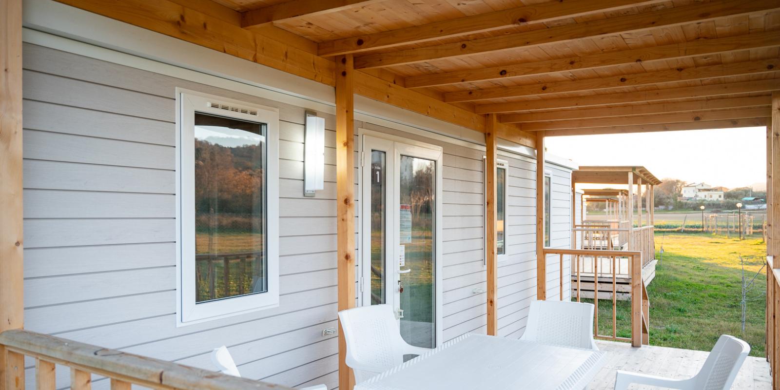 Veranda in legno con tavolo bianco e sedie, vista su prato verde.