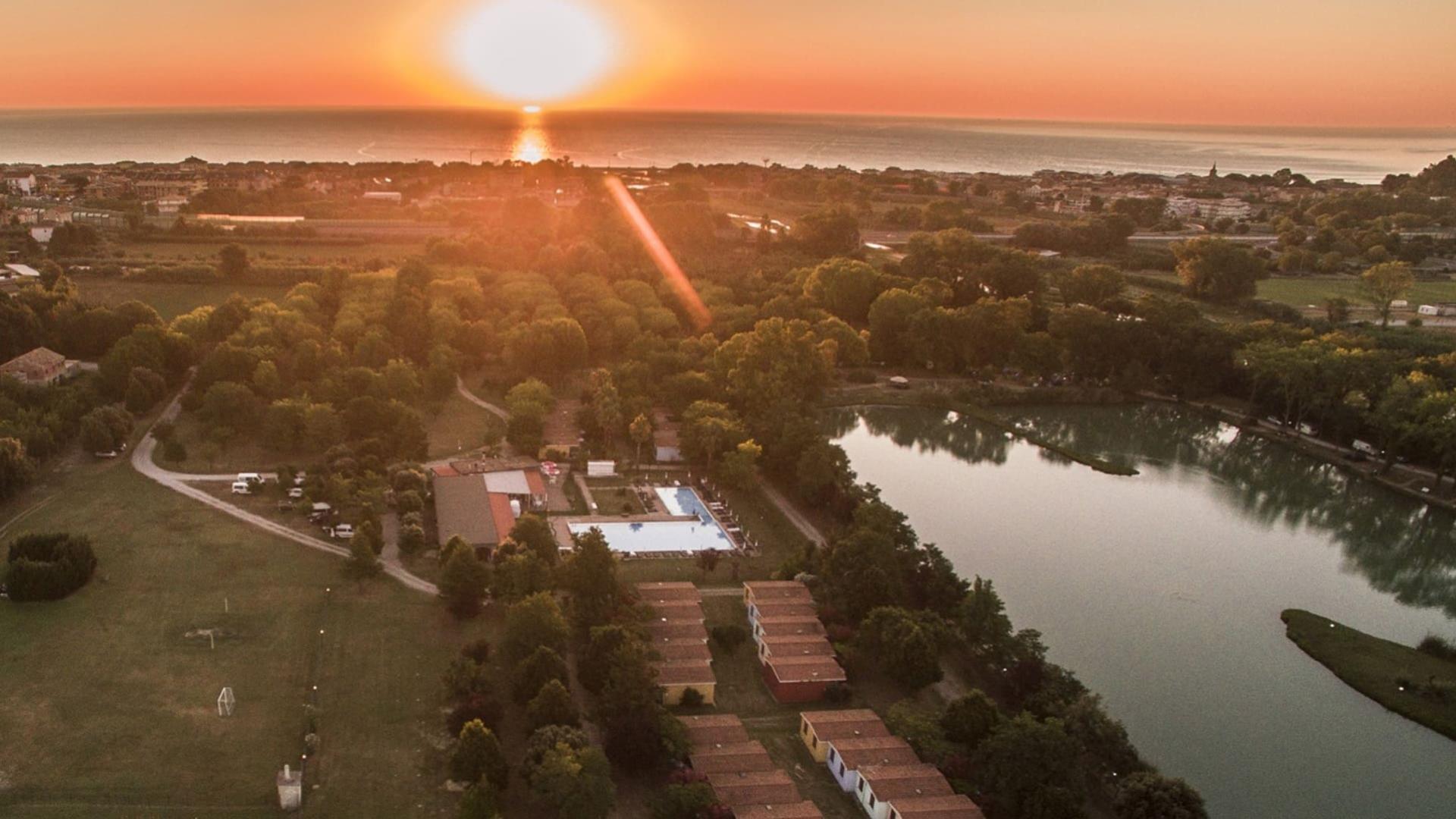 Tramonto su un villaggio con piscina, lago e vista sul mare.