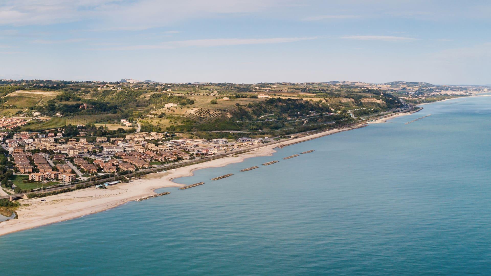 Vista panoramica di una costa con spiaggia, mare e colline sullo sfondo.