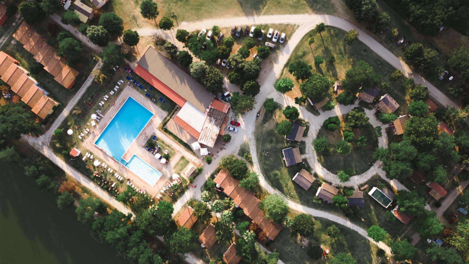 Vista aerea di un villaggio turistico con piscina, case e aree verdi.