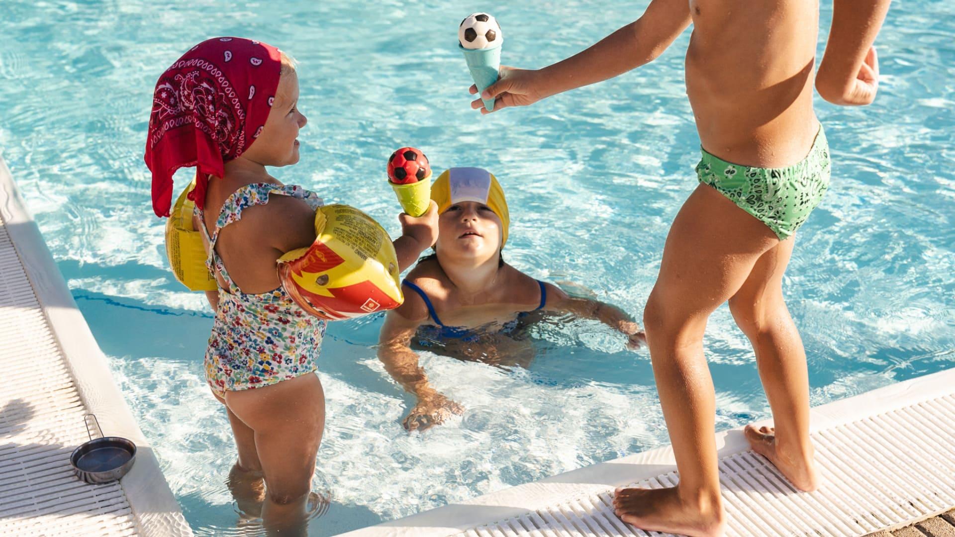 Bambini giocano in piscina con gelati a forma di pallone da calcio.