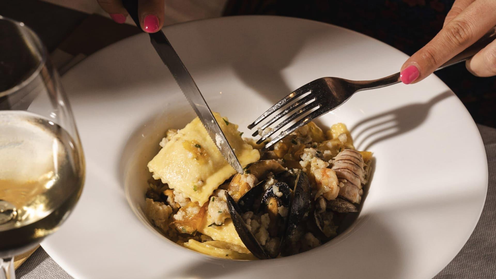 Piatto di ravioli di pesce con frutti di mare e un bicchiere di vino bianco.