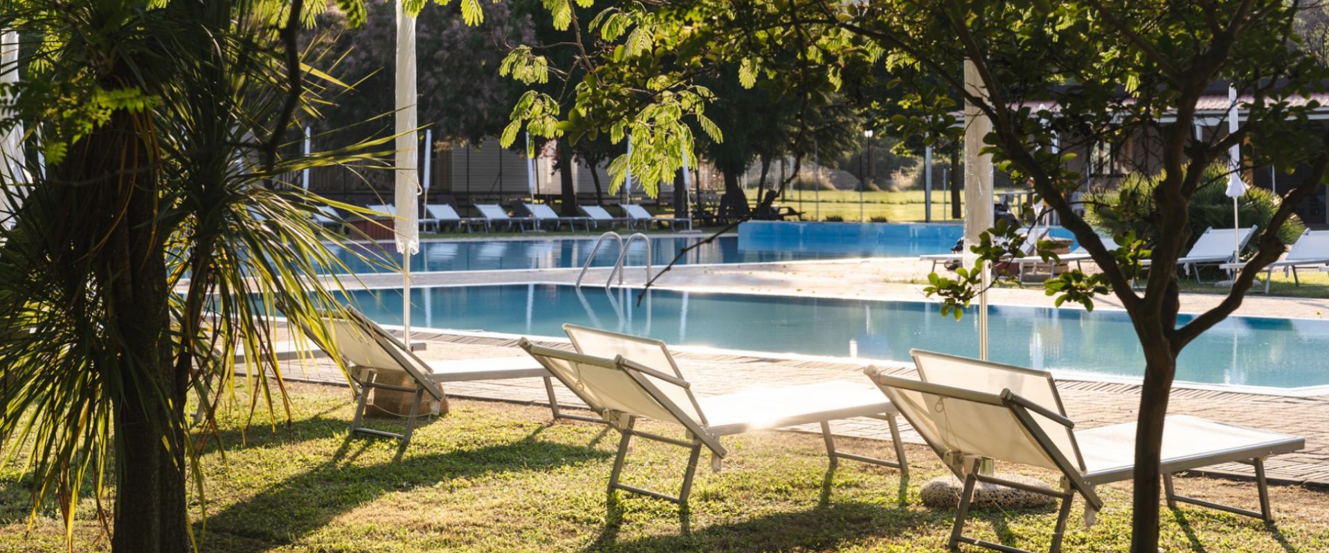 Piscina all'aperto con lettini e ombrelloni, circondata da alberi e vegetazione.