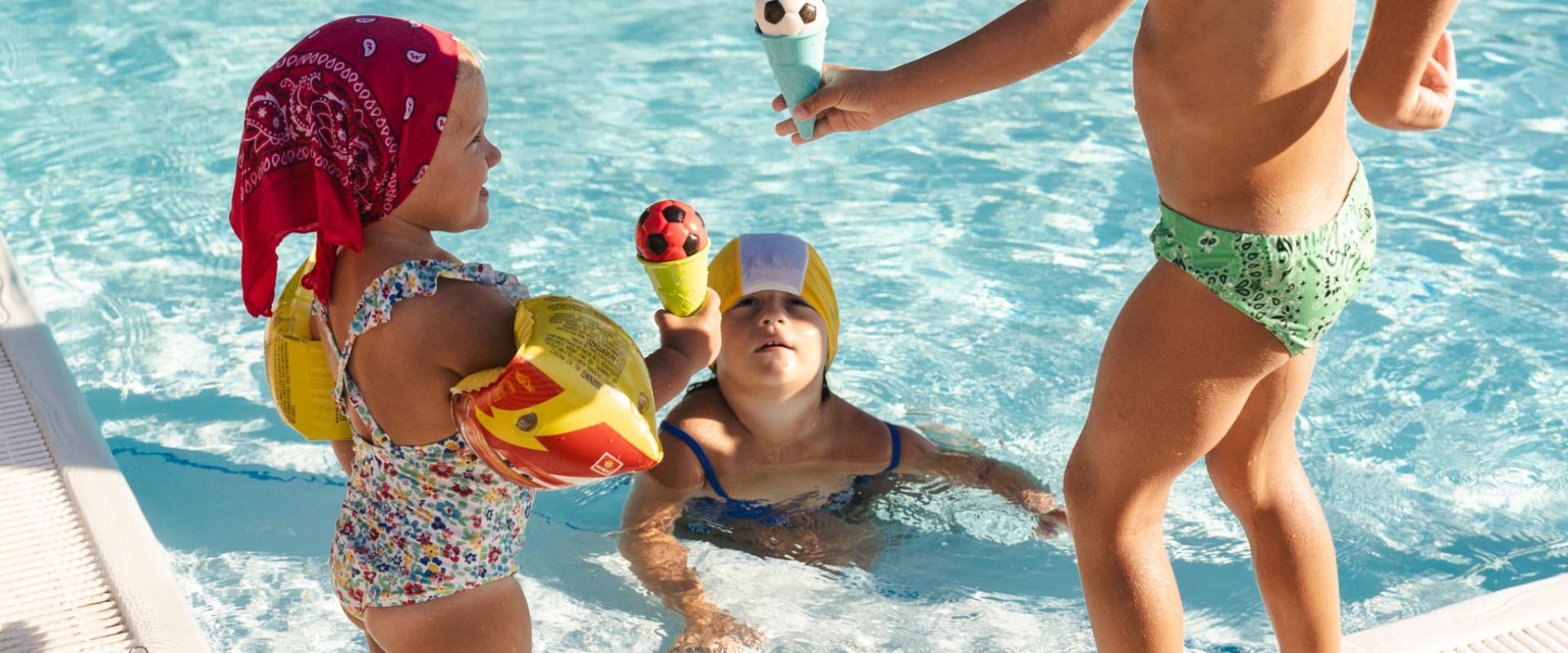 Bambini che giocano in piscina con giocattoli a forma di gelato e pallone.