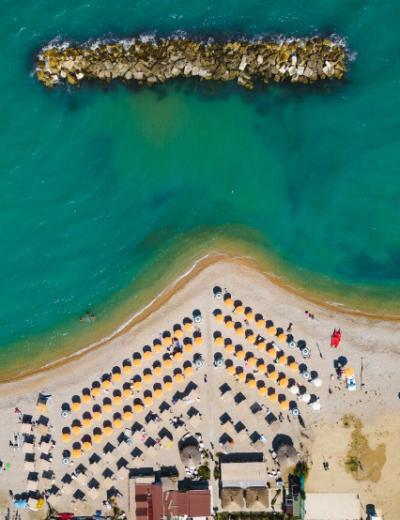 Spiaggia con ombrelloni gialli, mare turchese e barriera frangiflutti vista dall'alto.