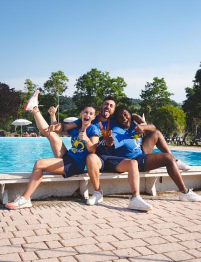 Tre amici felici posano davanti a una piscina, indossando magliette blu.