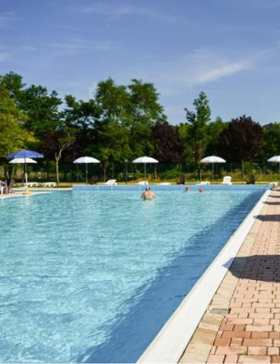 Donna legge un libro e beve un cocktail a bordo piscina su una sdraio.