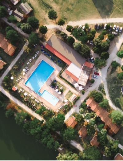 Vista aerea di un complesso con piscina, case e parcheggio immerso nel verde.