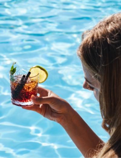 Persona con cocktail in mano vicino a una piscina.