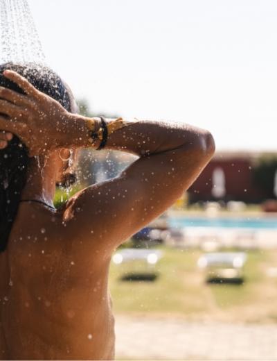 Persona sotto la doccia all'aperto vicino a una piscina in una giornata soleggiata.