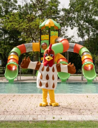 Personaggio in costume da gallina davanti a scivoli colorati in un parco acquatico.