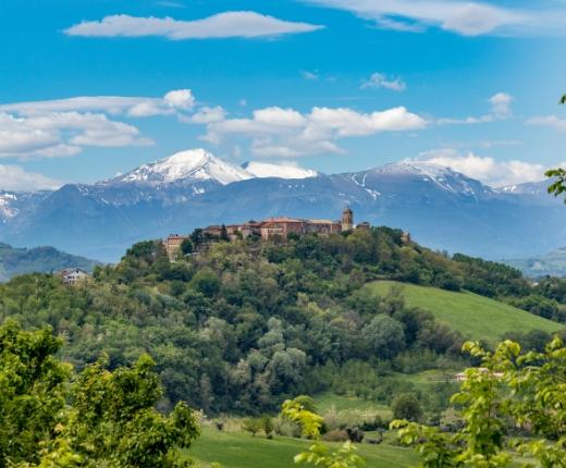 Un borgo collinare con vista sulle montagne innevate, immerso nel verde della natura.