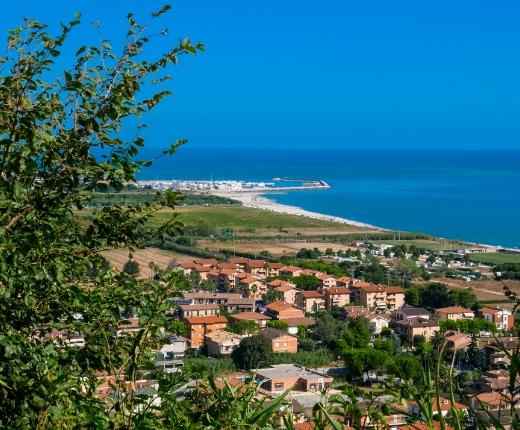 Vista panoramica di una città costiera con case, vegetazione e mare azzurro.