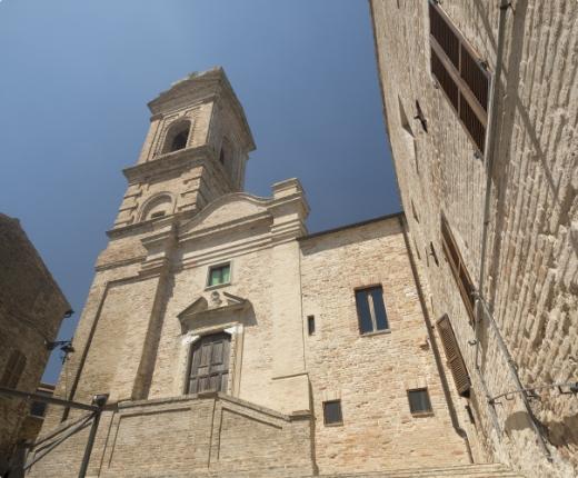 Chiesa storica in mattoni con campanile, situata in una stretta via di un borgo.