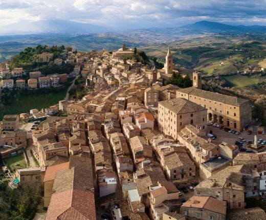 Vista aerea di un pittoresco borgo italiano con edifici storici e paesaggio collinare.