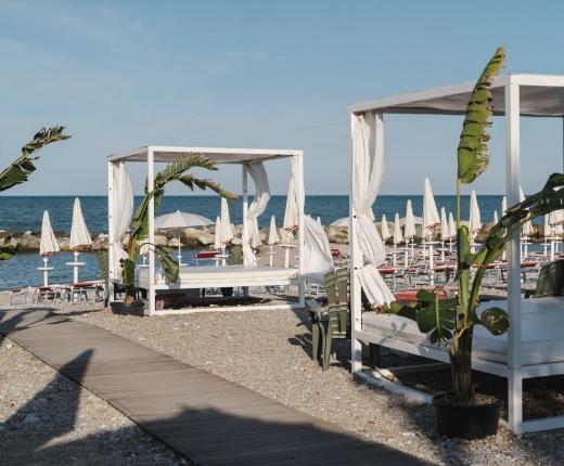 Spiaggia con lettini bianchi, ombrelloni chiusi e vista sul mare.