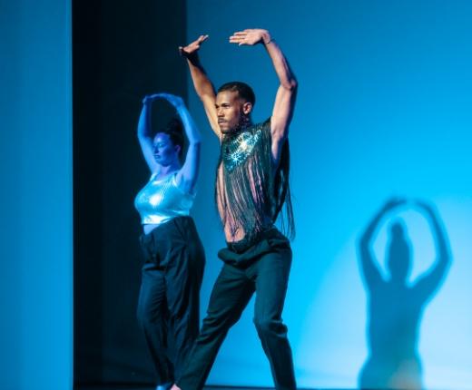 Due ballerini eseguono una coreografia con costumi brillanti su sfondo blu.