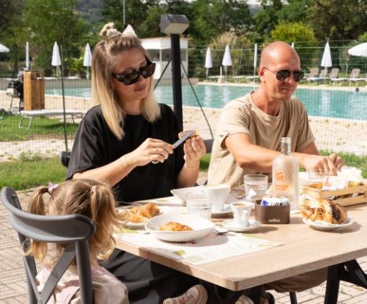 Famiglia fa colazione all'aperto vicino alla piscina in una giornata soleggiata.