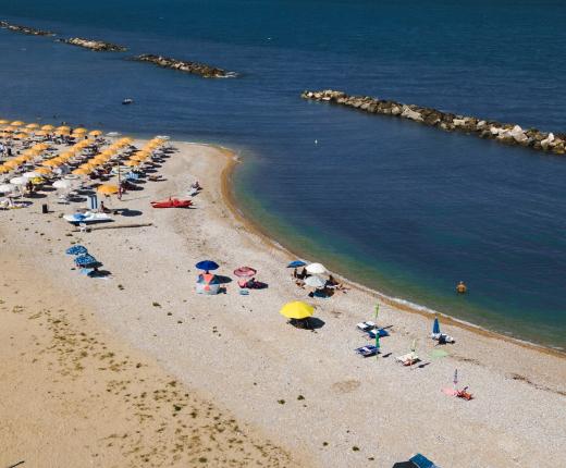 Spiaggia con ombrelloni colorati e palme, vicino al mare calmo e frangiflutti.