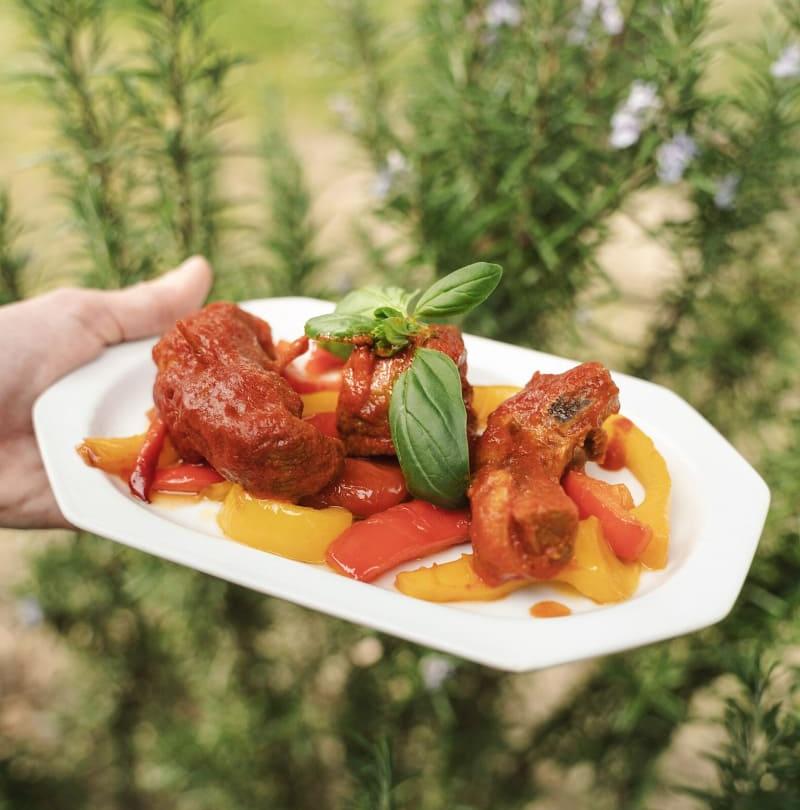 Piatto di carne con peperoni rossi e gialli, guarnito con foglie di basilico.