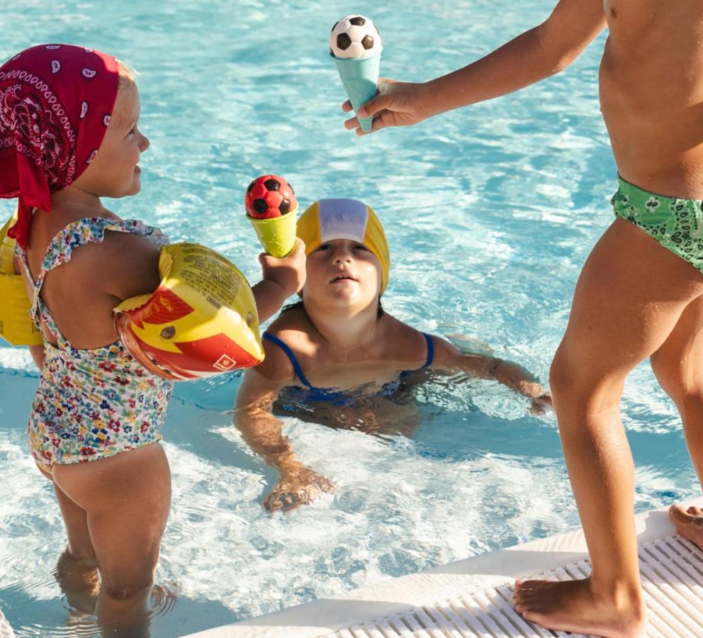 Bambini giocano in piscina con gelati a forma di pallone da calcio.